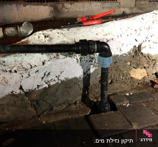 צינור שחור עם מחבר פלסטיק כחול על קיר לבן